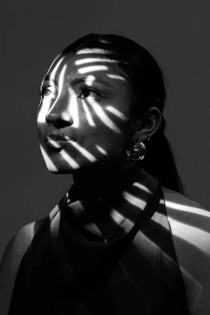 Light through blinds across her face, in black and white