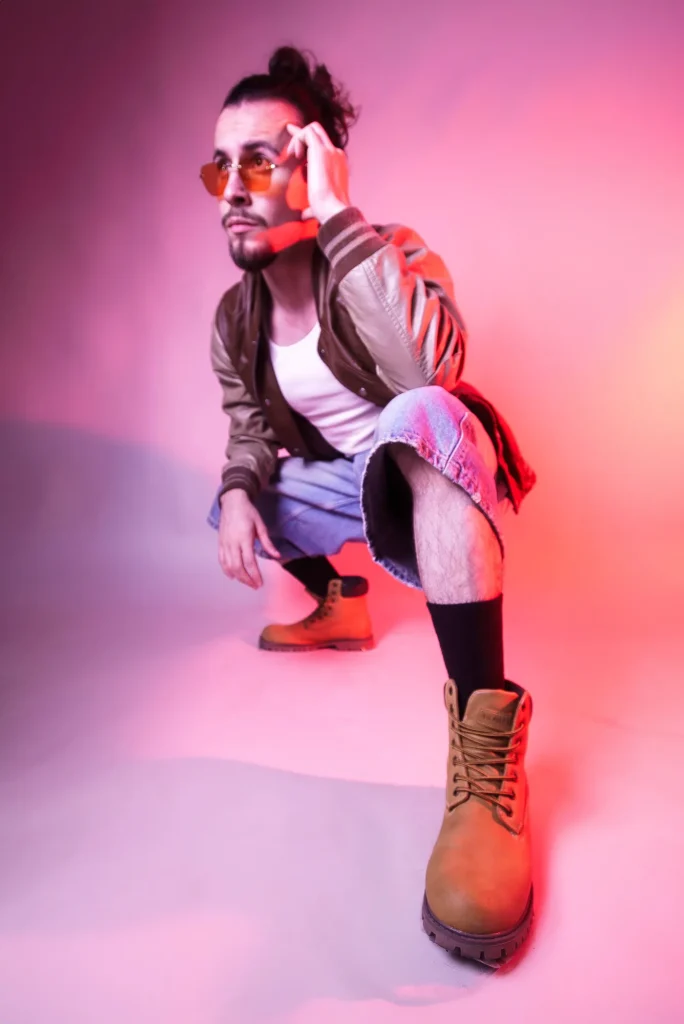 Crouched in pink light, sunglasses and boots