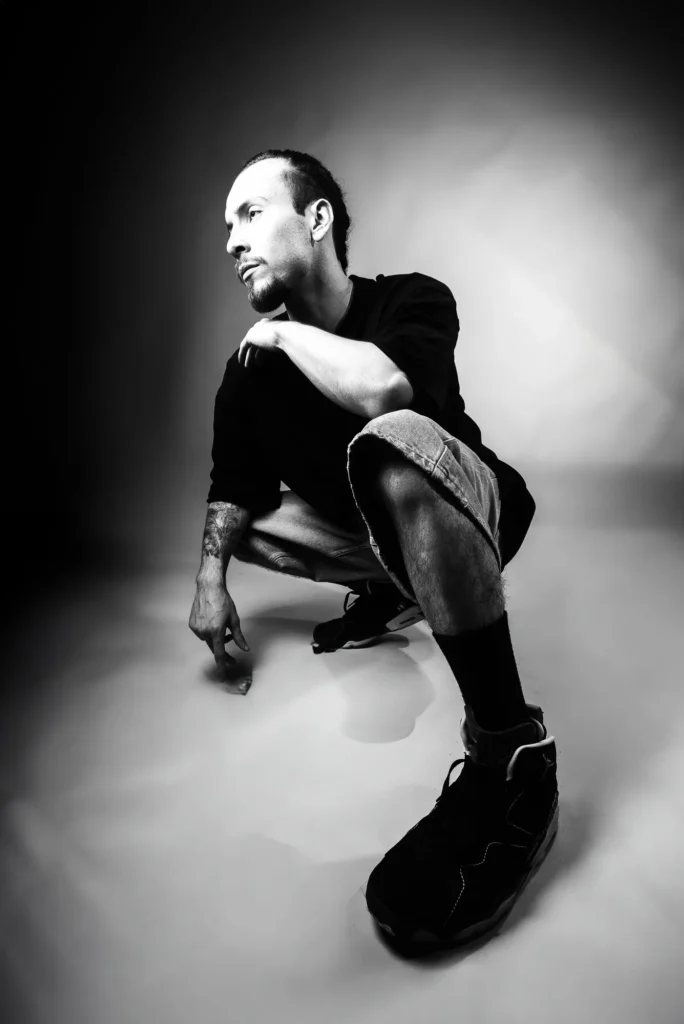 Crouched in a white studio, in black and white