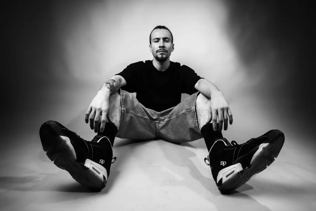 Seated on a white floor, sneakers forward