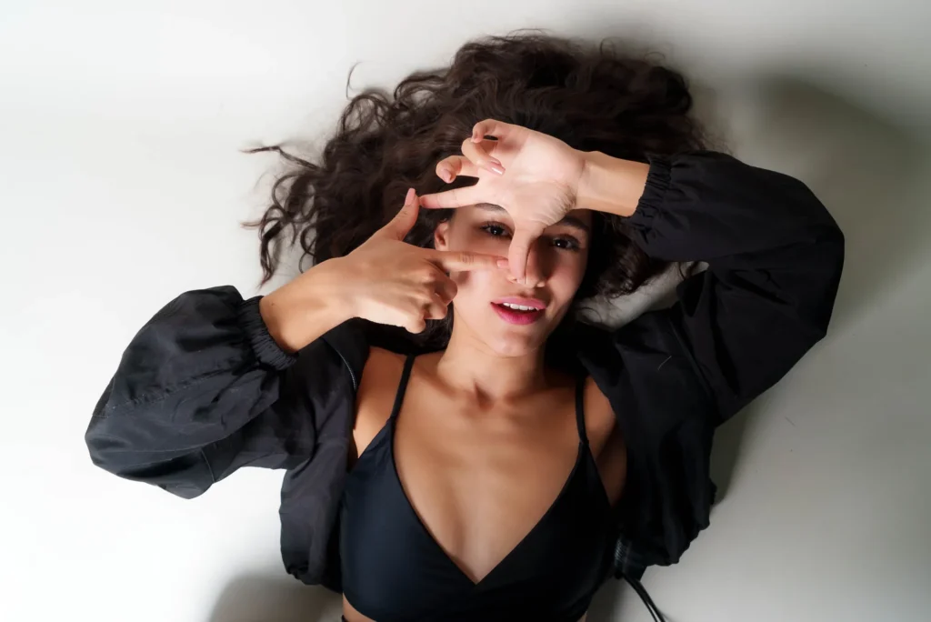 Lying down, framing her eye with her hands
