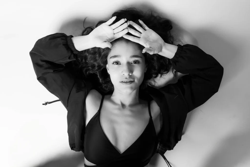 Lying down, hands on her head, in black and white