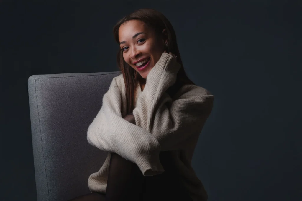 Laughing in a knit sweater, on a gray chair