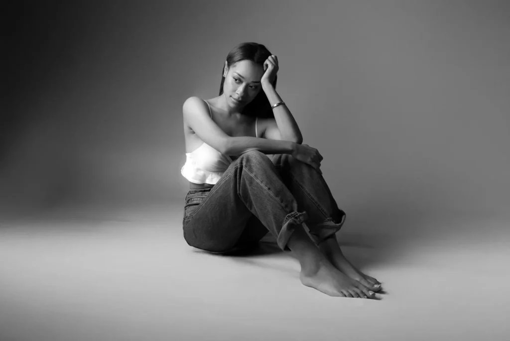 Seated barefoot in jeans, in black and white