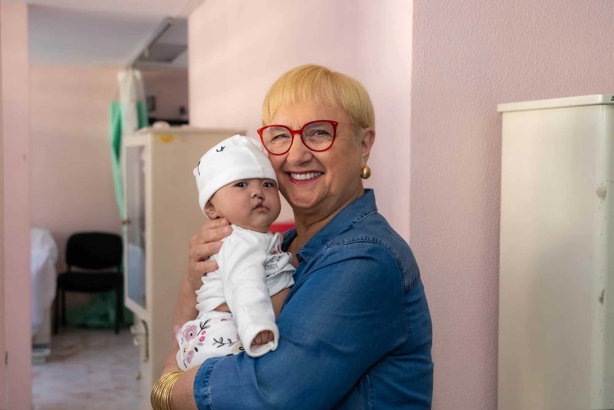 Lidia holds a baby in a pink room