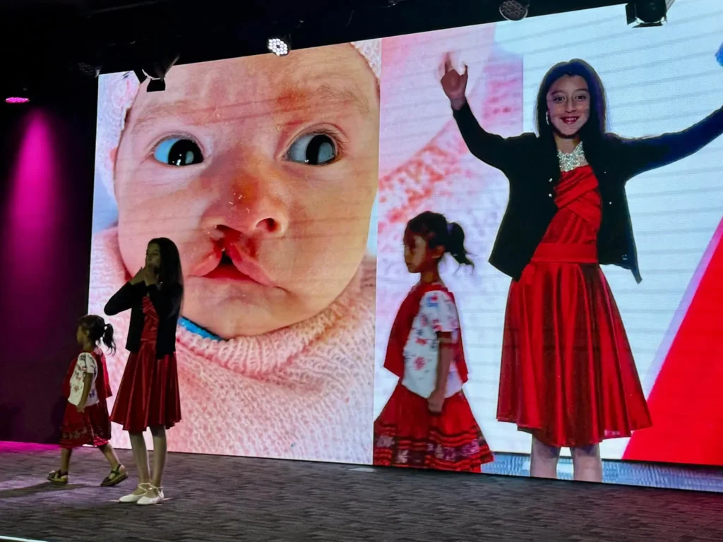A girl on stage in front of her baby photo, projected on the screen