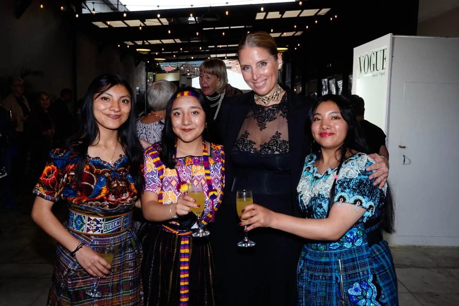 Young women in traditional dress raise a toast with a guest