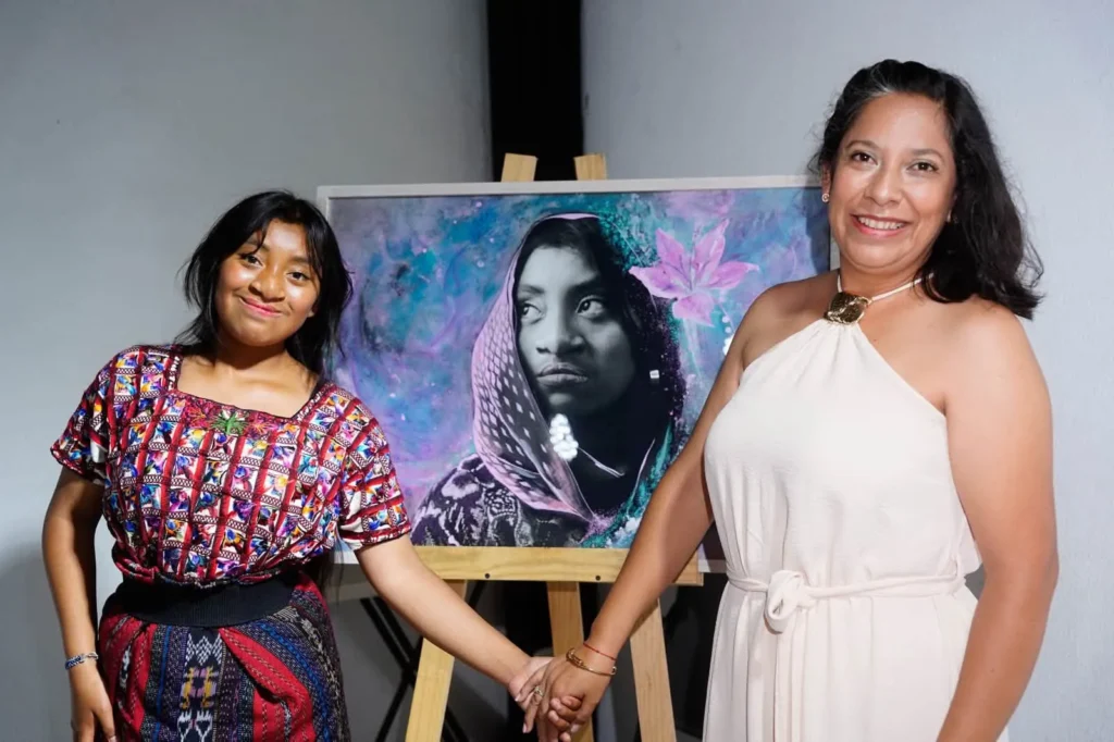 A young woman and a woman hold hands in front of a painted portrait